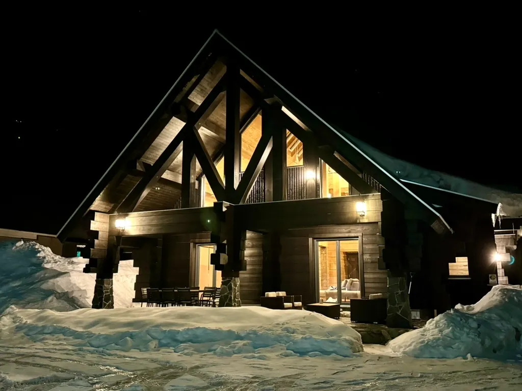 雪景色の中にたたずむログハウス。窓から漏れる光が美しい冬の夜の風景。